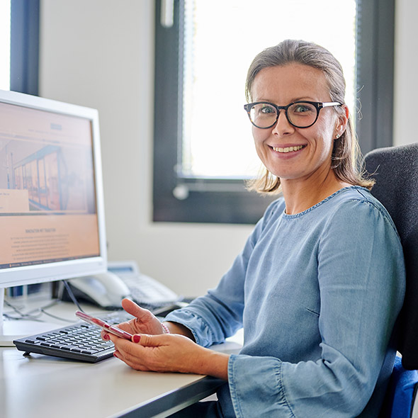 A woman in glasses working at a desk with a computer in front of her