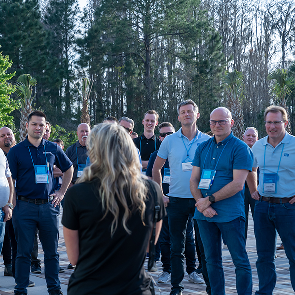 A diverse group of individuals standing togther and listening to a lady